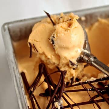 Ice cream scoop holding a scoop of orange butterscotch ice cream.