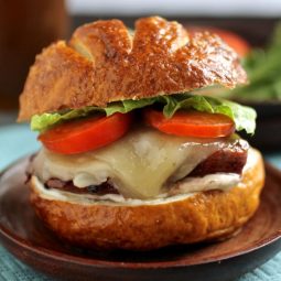 Chicken on a pretzel roll with tomatoes and lettuce.