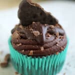 Chocolate cupcake in a green wrapper, topped with chocolate frosting and half of a thin mint cookie.