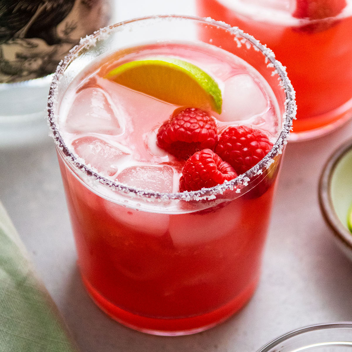 Margarita in a short glass, topped with fresh raspberries and a lime wedge.