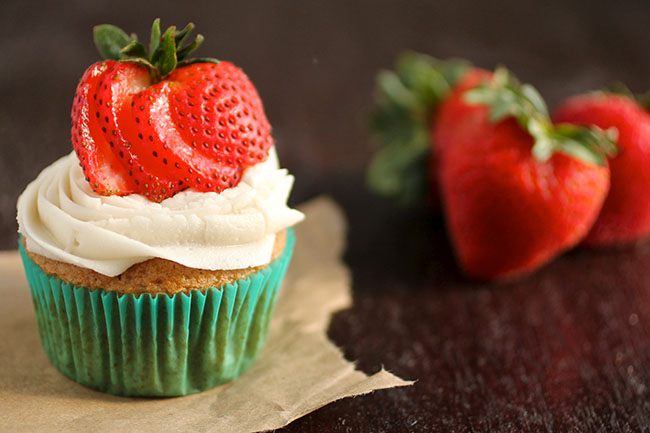 Vanilla cupcake topped with sliced strawberries, next to several fresh strawberries.