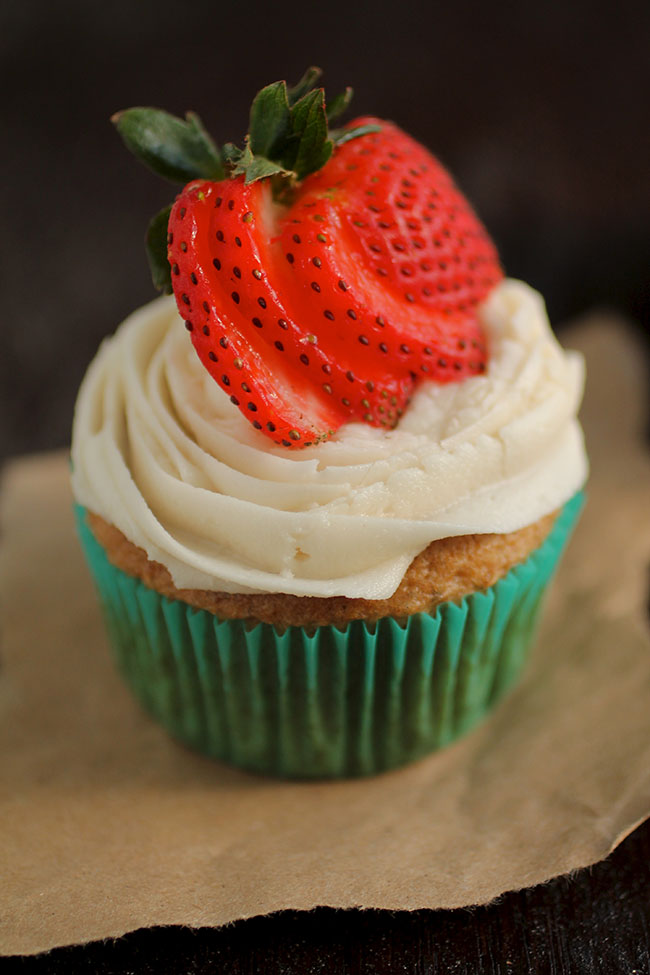 Vanilla cupcake topped with sliced strawberries.