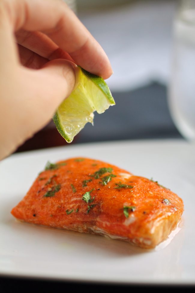 Hand squeezing a lime wedge over a piece of salmon.
