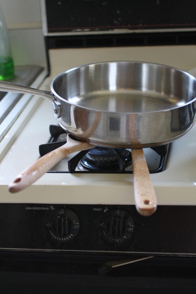 A large saucepan sitting on top of two wooden spoons to hold them in place.