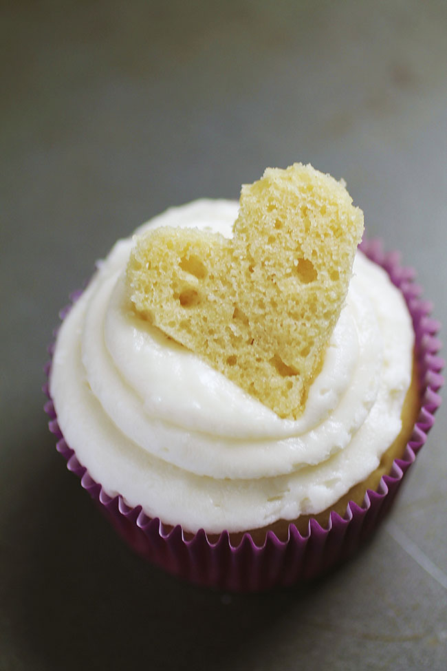 Vanilla cupcake topped with a piece of cake cut into the shape of a heart.