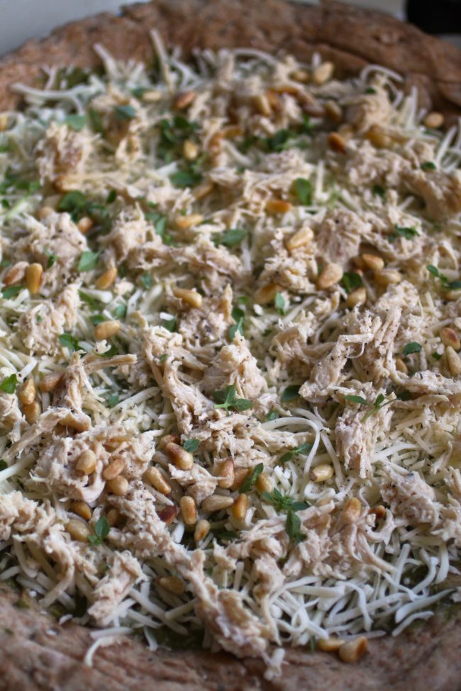 Pizza dough topped with shredded chicken, herbs, and pine nuts.