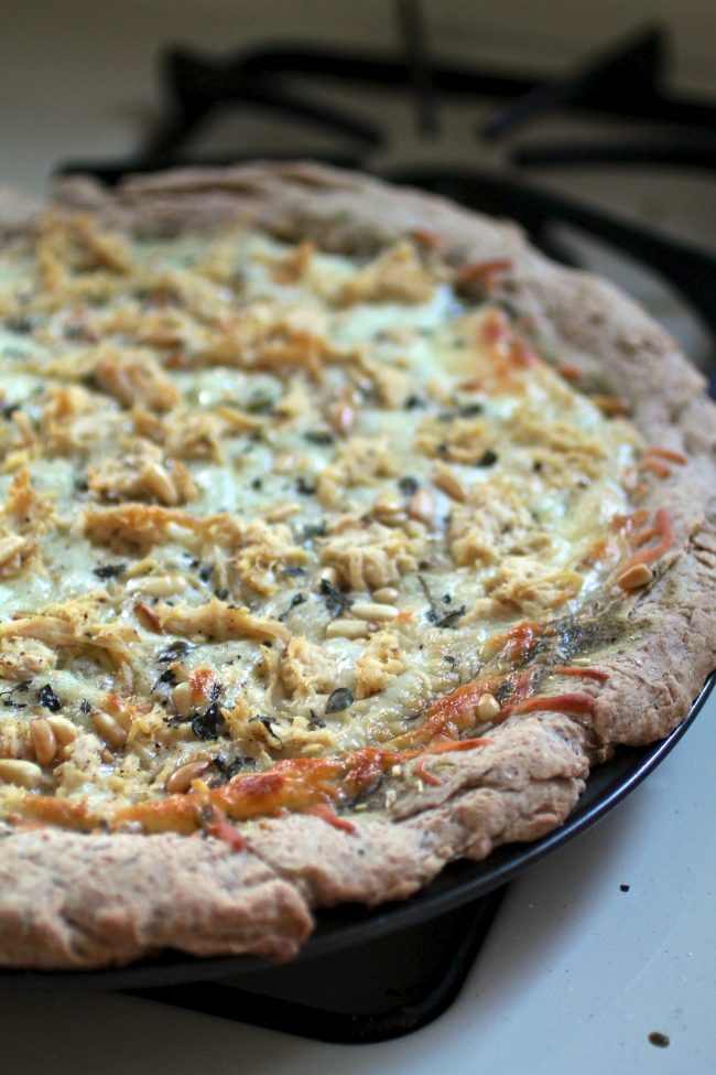 Whole pizza topped with cheese and shredded chicken, sitting on a pizza pan.