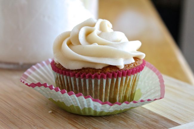 Vanilla cupcake with vanilla frosting on a wooden cutting board.