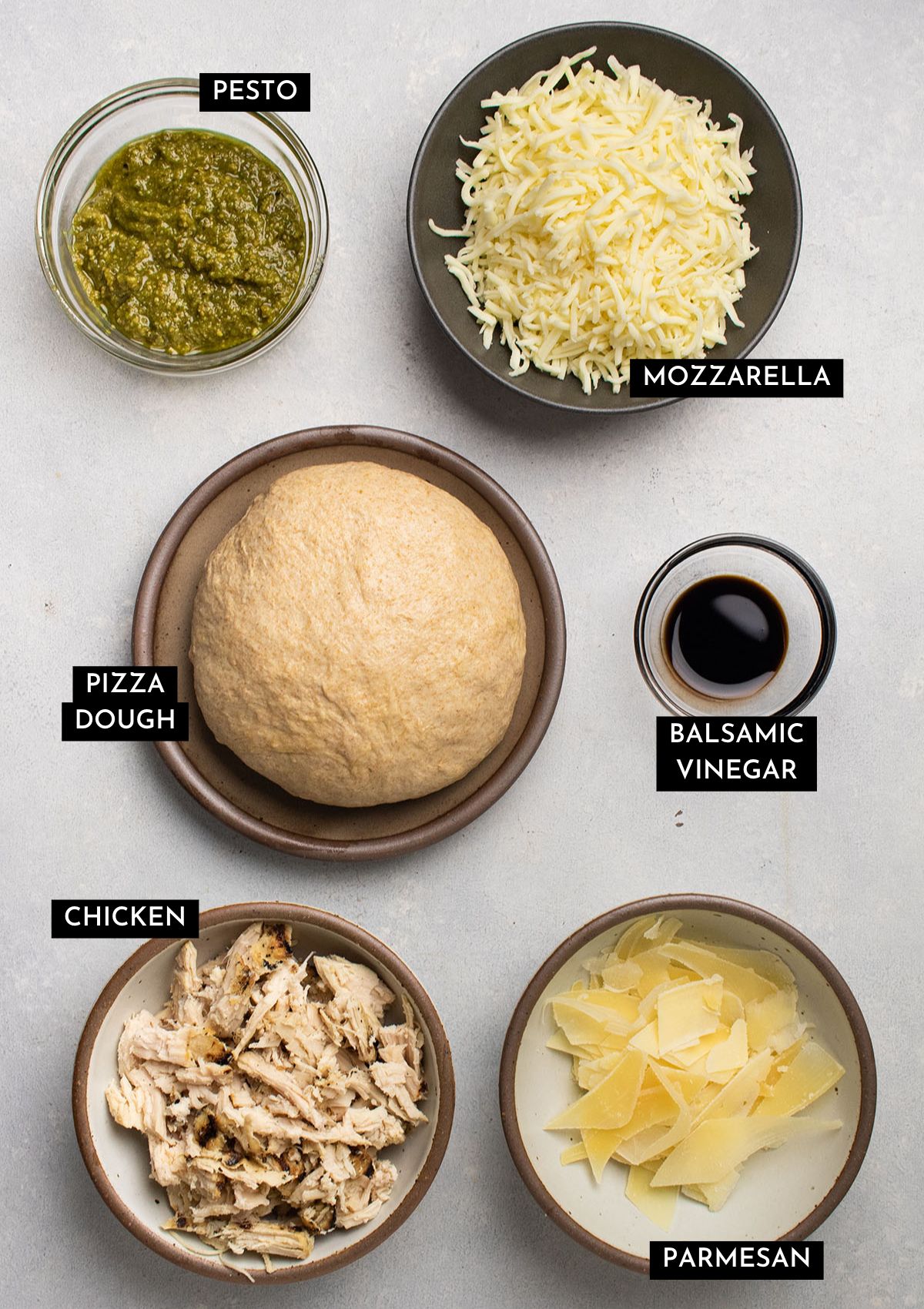 Pizza ingredients, organized into individual bowls on a white table.