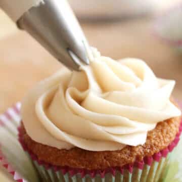 Piping bag putting vanilla frosting on a cupcake.
