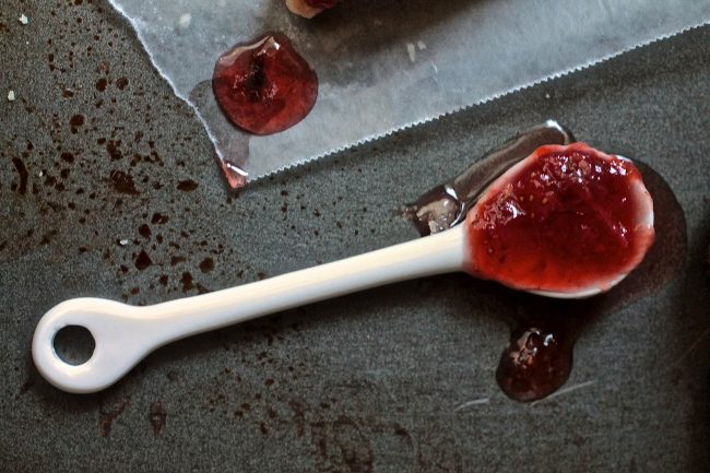 Strawberry jam on a white ceramic spoon.