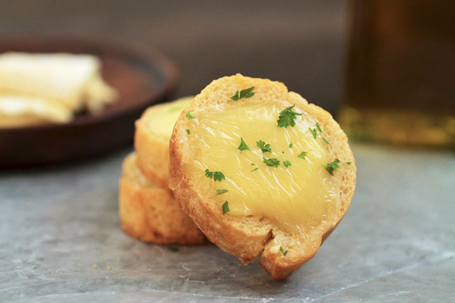 Close up of crostini topped with melted brie and fresh parsley.