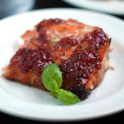 A piece of salmon topped with strawberry jam and fresh basil, sitting on a white plate.