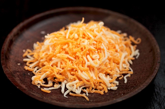 Shredded cheddar cheese on a small wood plate.
