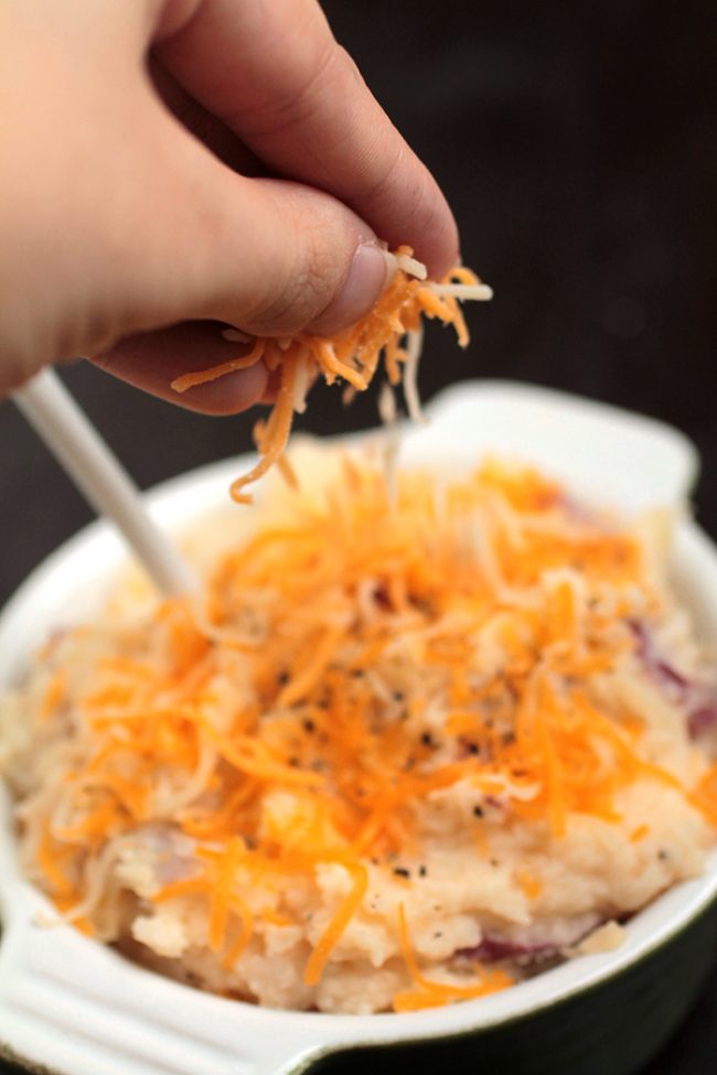 Hand sprinkling shredded cheese over mashed potatoes.