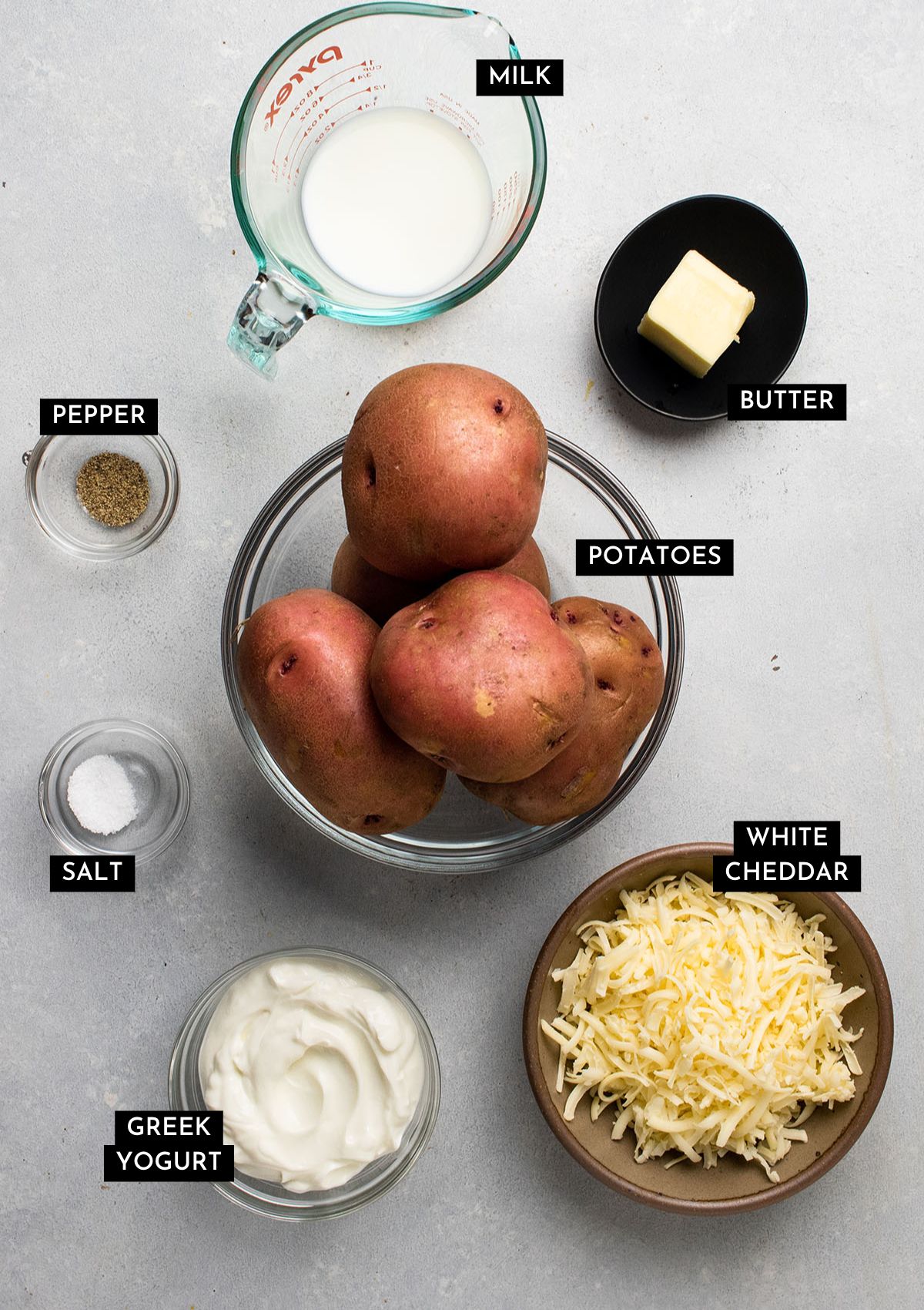 Red potatoes, cheddar cheese, and greek yogurt in small bowls on a white table.
