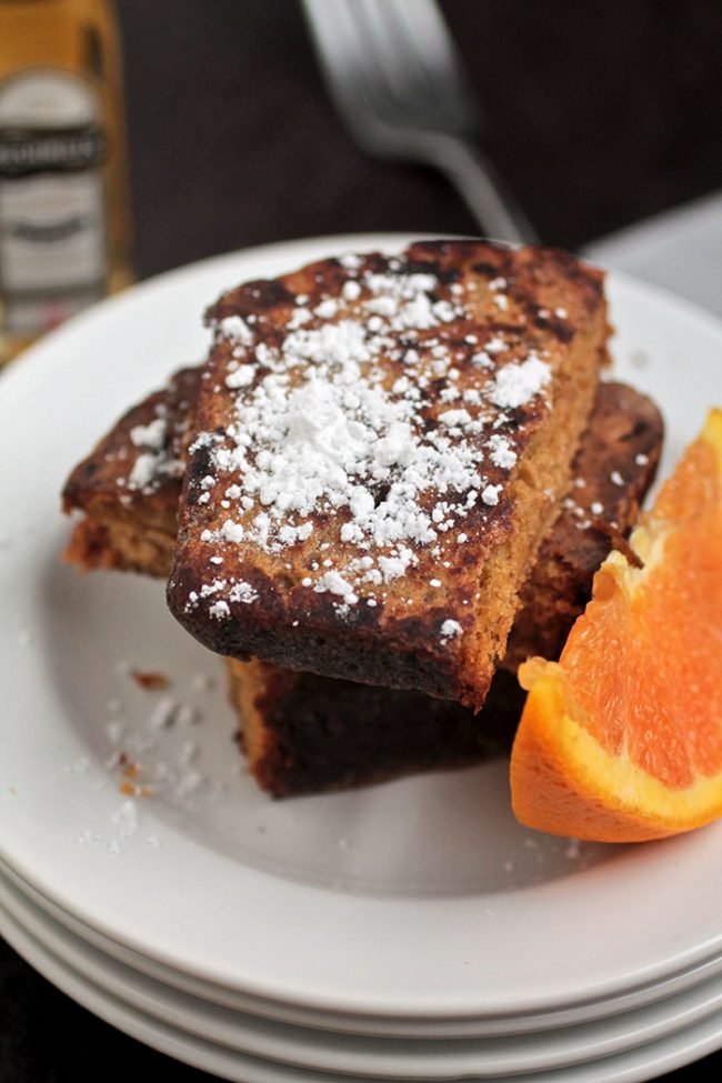 French toast slices on a white plate, next to an orange slice.