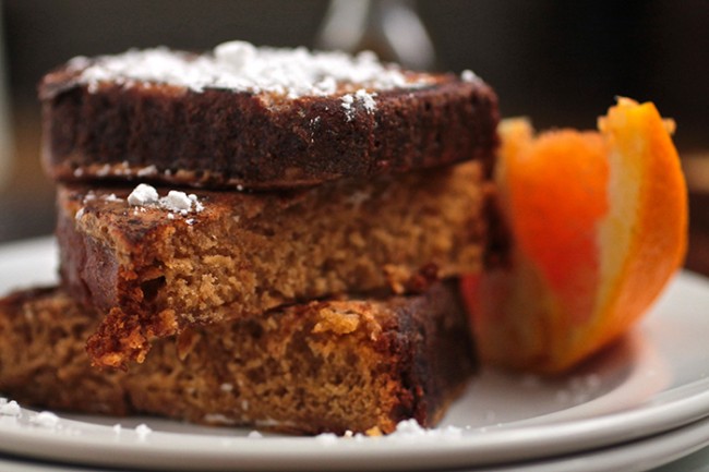 Close up of a stack of three pieces of french toast next to an orange slice.