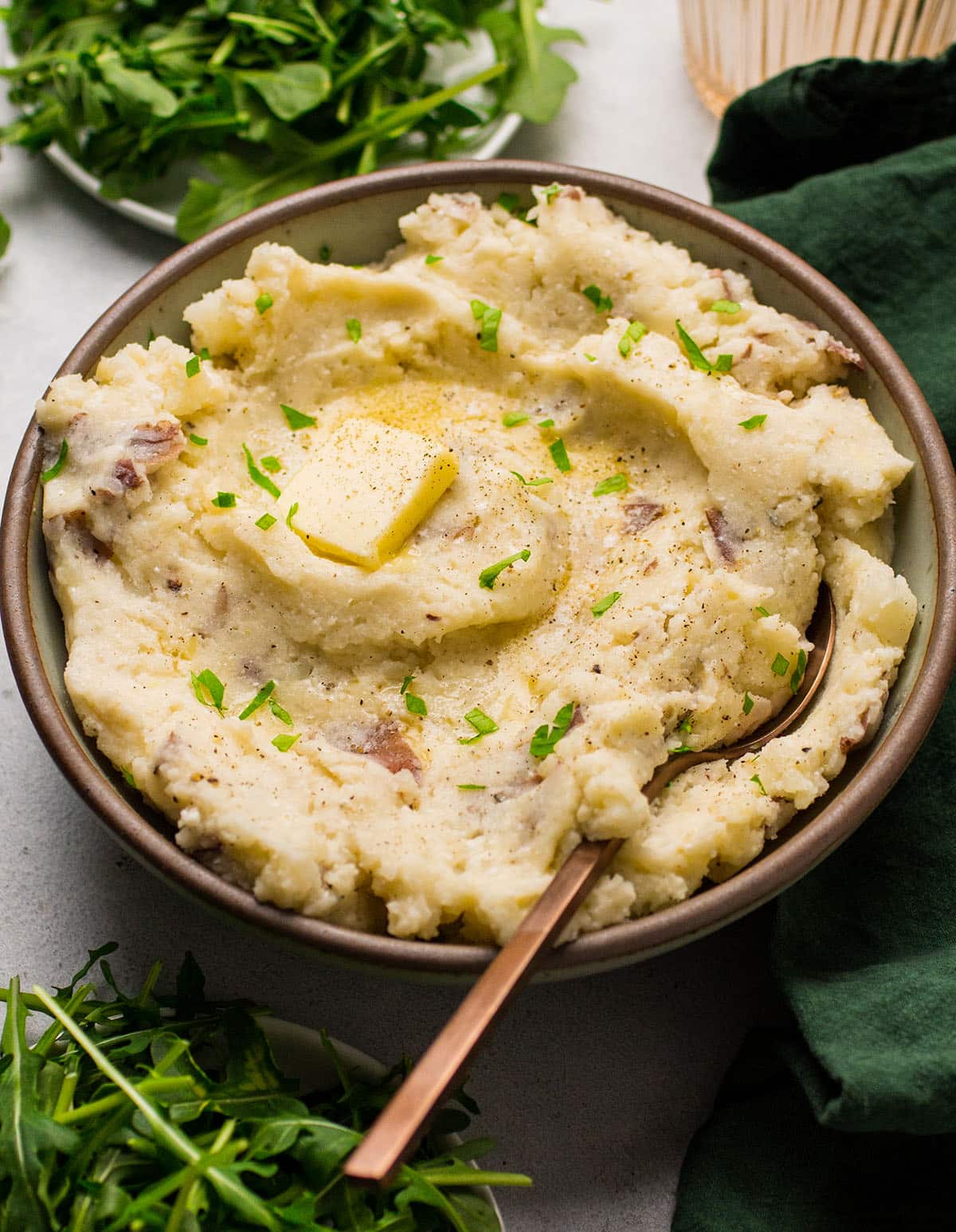 White cheddar potatoes in a shallow bowl with a copper spoon.