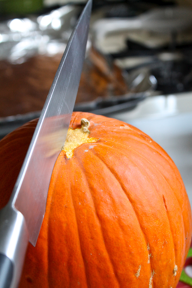 Slicing a pie pumpkin in half with a large knife.