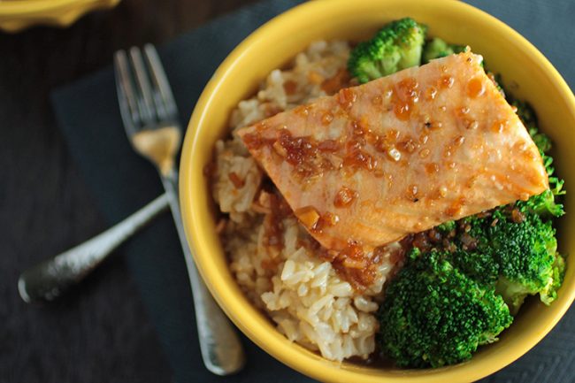 A piece of teriyaki salmon sitting on top of brown rice and steamed broccoli.