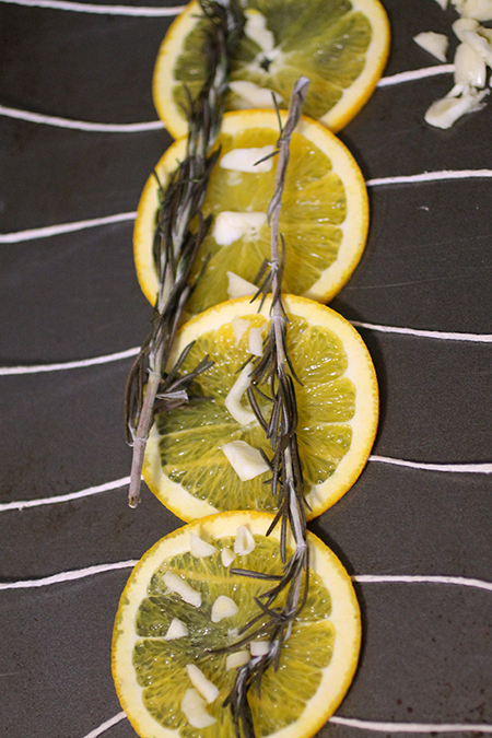 Orange slices and fresh rosemary laying across a line of kitchen twine on a baking sheet.