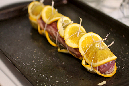 Pork tenderloin and orange slices tied with kitchen twine.