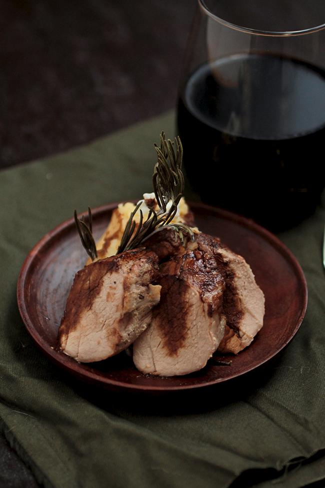 Pork tenderloin slices and mashed potatoes on a small wooden plate.