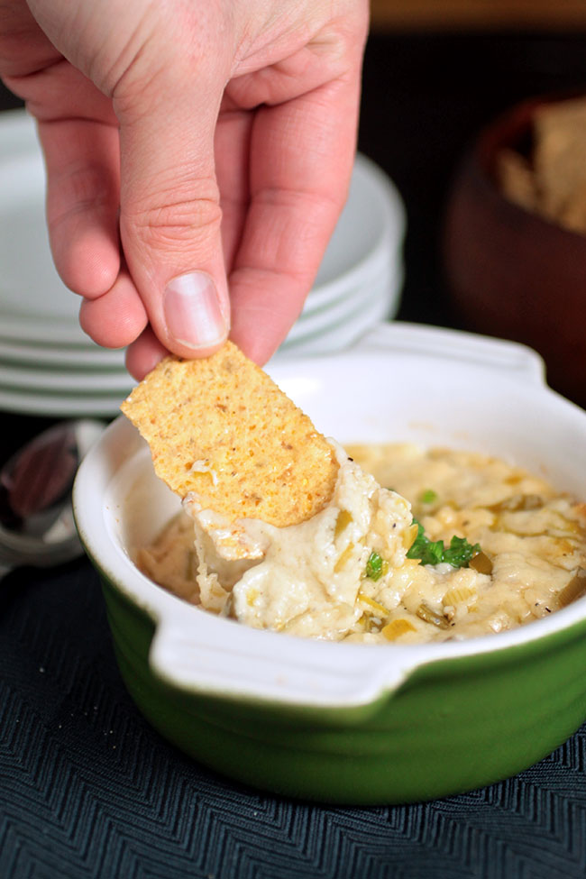 Hand dipping a tortilla chip into a small bowl filled with cheese dip.