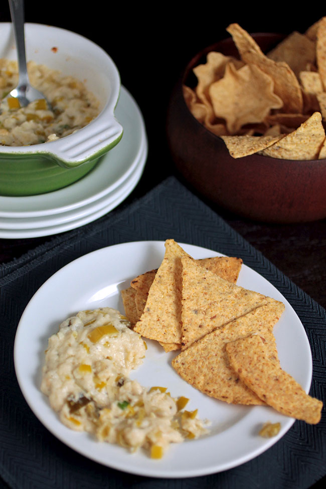 Cheese dip, tortilla chips, and a white appetizer plate on a brown table.