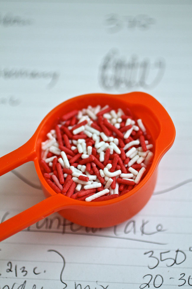 Orange measuring cup filled with white and red sprinkles.