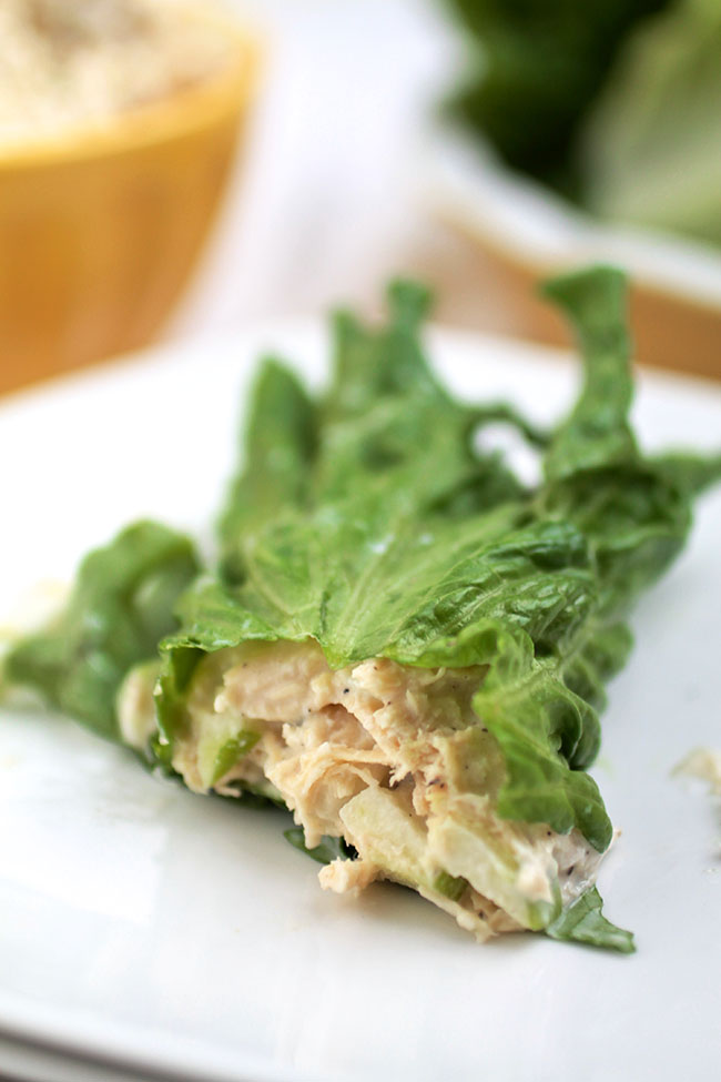 A scoop of chicken salad wrapped in a lettuce leaf, on a white plate.