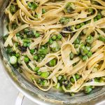 Fettuccine noodles in a silver pot with chopped asparagus and green peas.