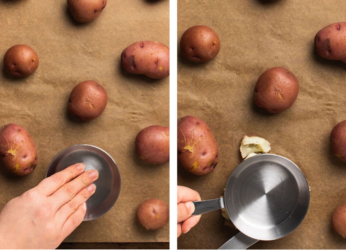 Smashing cooked potatoes on a baking sheet with a silver measuring cup.