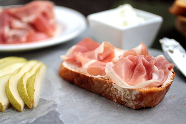 A piece of toast topped with goat cheese and prosciutto. 
