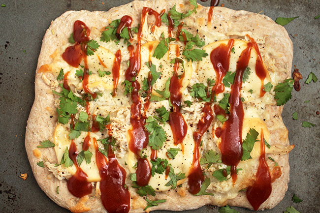 Overhead view of a rectangular pizza topped with barbecue sauce and fresh cilantro.