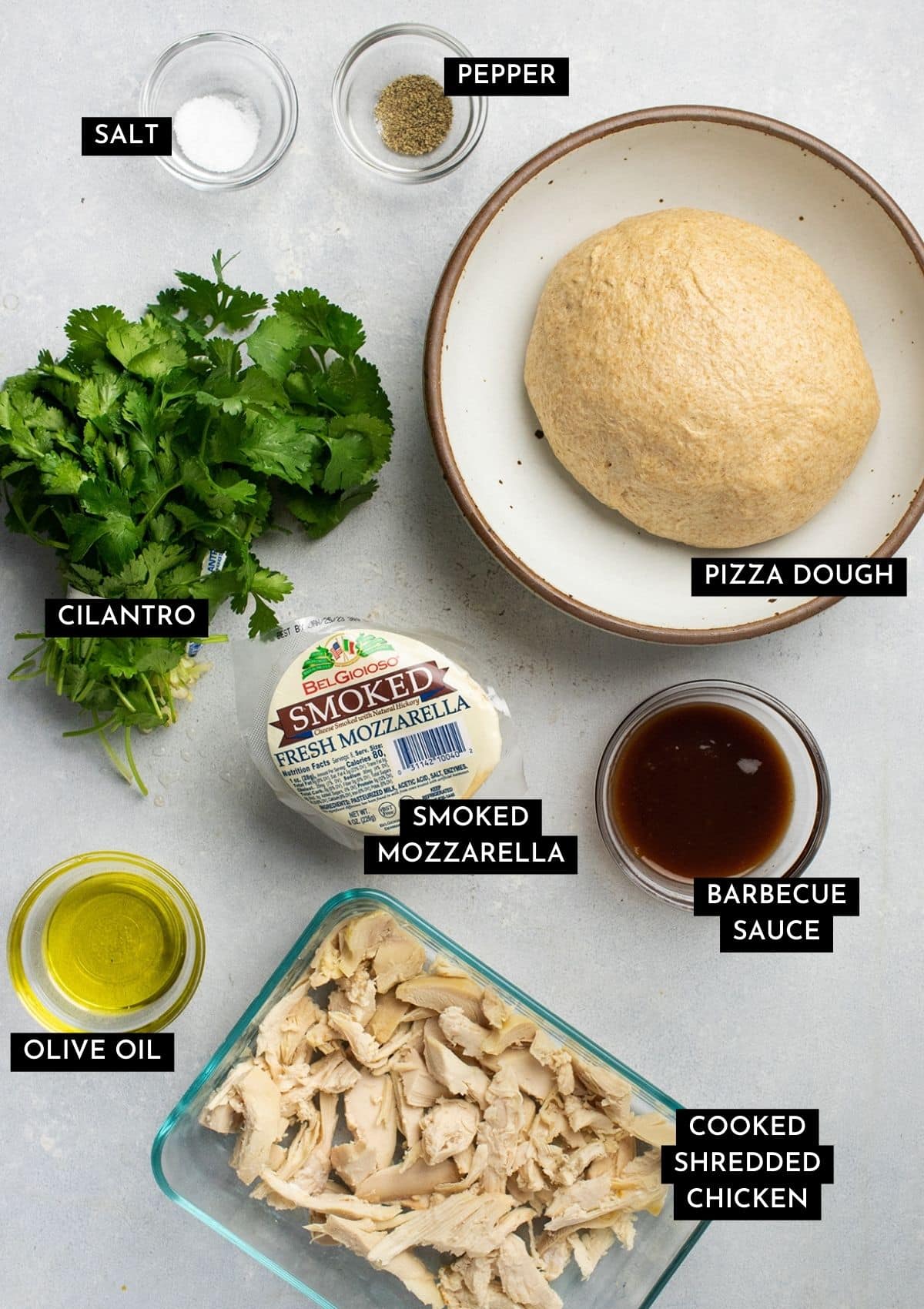 Pizza dough, chicken, cilantro, and other ingredients on a white table.