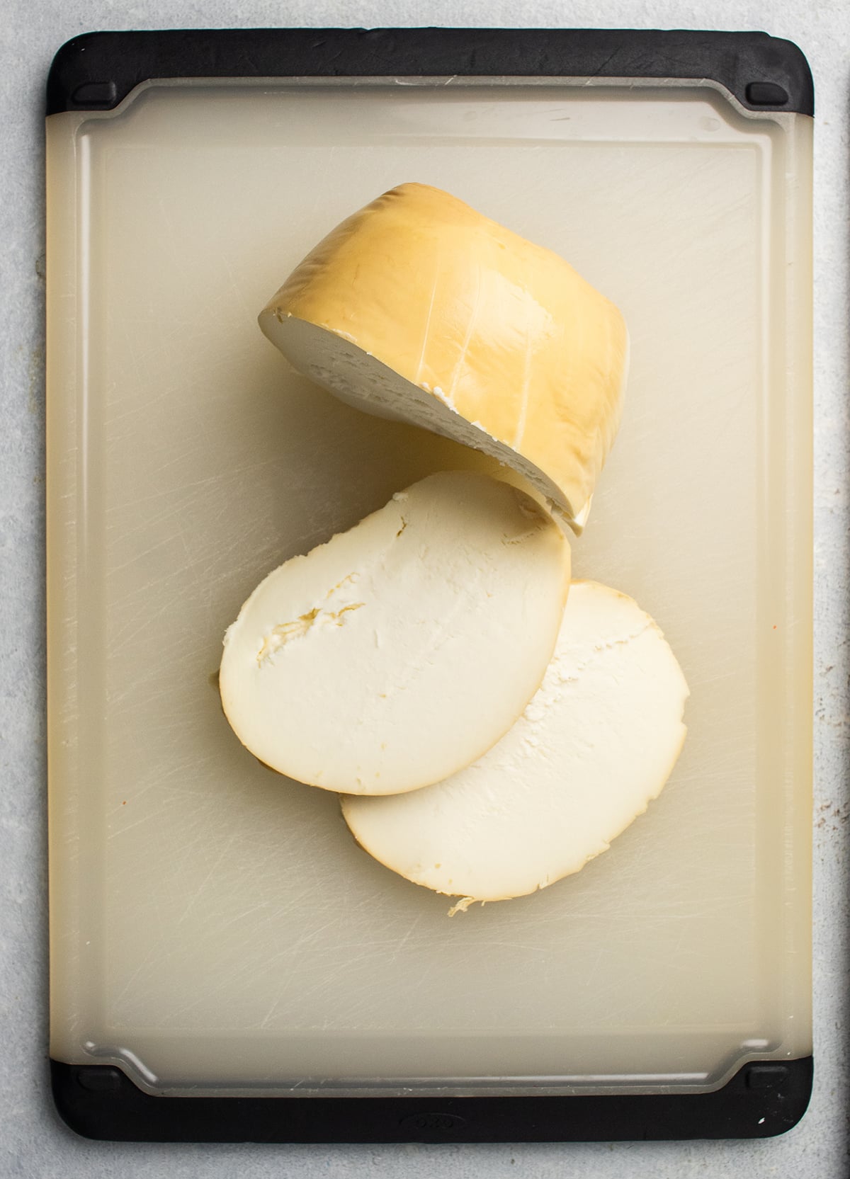 Smoked mozzarella cheese, cut into slices on a white cutting board.