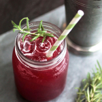 Blackberry whiskey lemonade in a mason jar filled with ice, topped with a striped paper straw and a sprig of fresh rosemary.