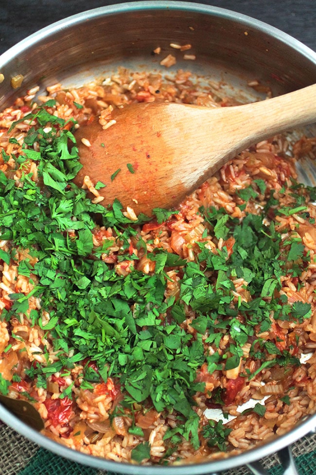 Wooden spoon stirring fresh chopped cilantro into a skillet of jambalaya.