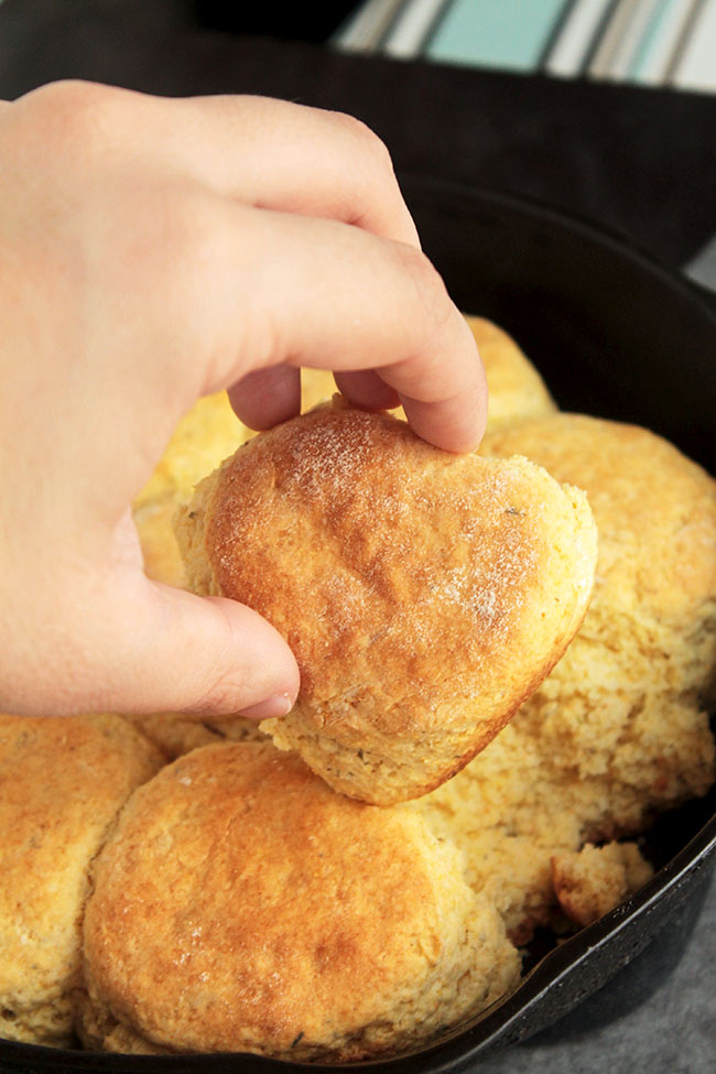 Hand pulling a cornbread biscuit out of a cast iron skillet.