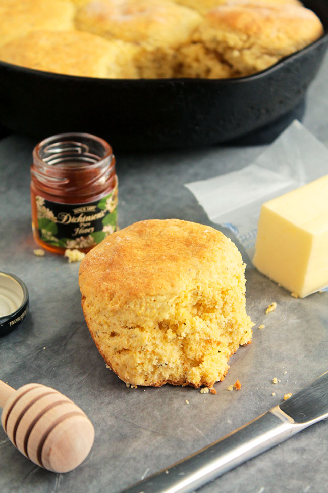Cornbread biscuit on a table next to a stick of butter and a jar of honey.