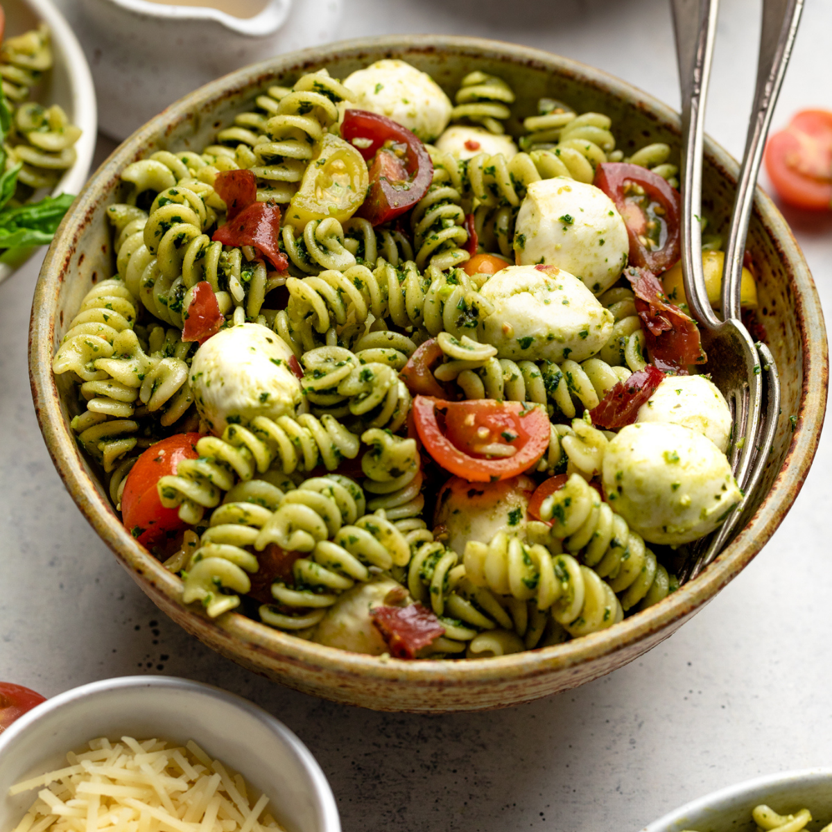 Pasta salad in a brown bowl with two serving spoons tucked into the side.