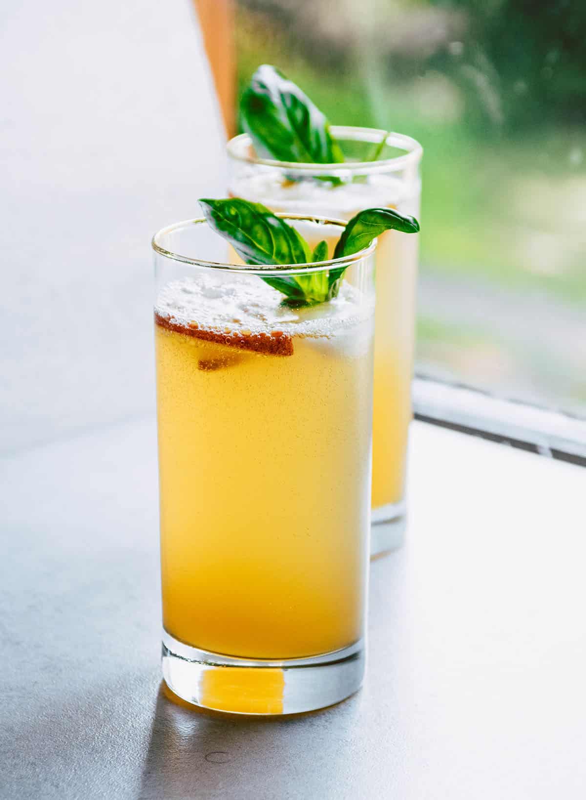 Two peach spritzers in tall glasses topped with fresh basil sprigs.