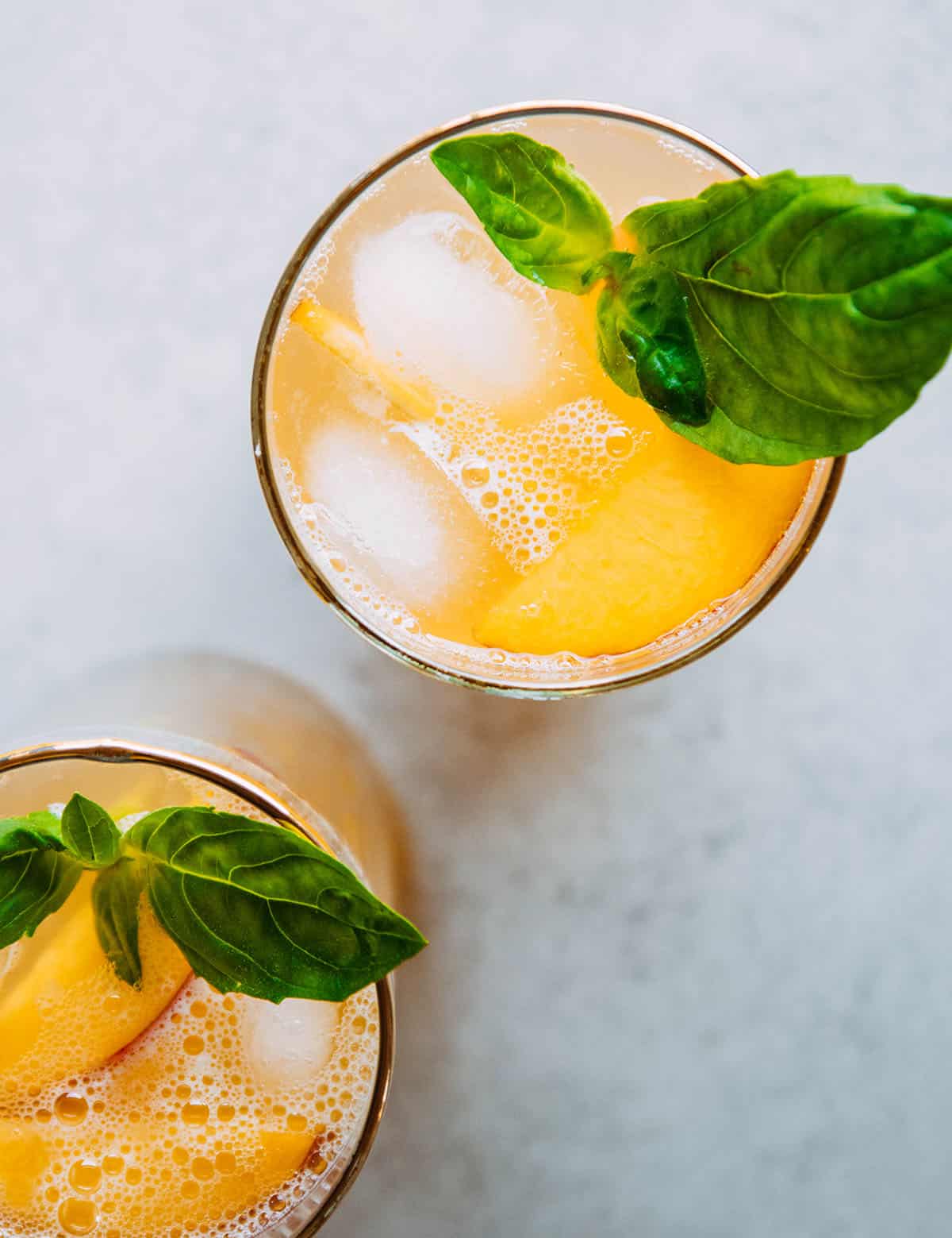 Peach cocktail in a gold-rimmed glass with sliced peaches and basil garnish.