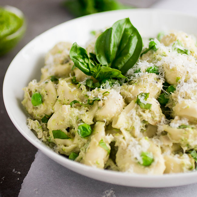 Pesto tortellini in a shallow white bowl, topped with fresh basil and shredded parmesan.