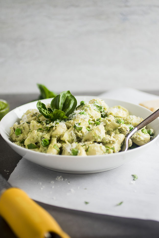 White bowl filled with tortellini and fresh peas, with a wooden fork on the side.