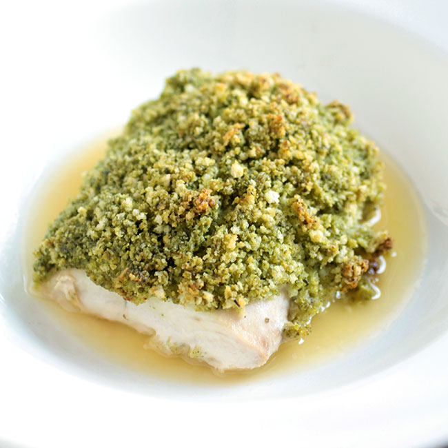 Mahi Mahi with a pesto crust, sitting in a pool of butter on a white plate.