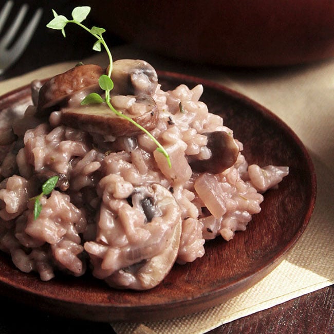 Light pink risotto and a sprig of fresh thyme on a dark wooden plate.