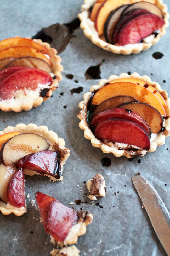 Three small tart shells topped with stone fruit on a light background.